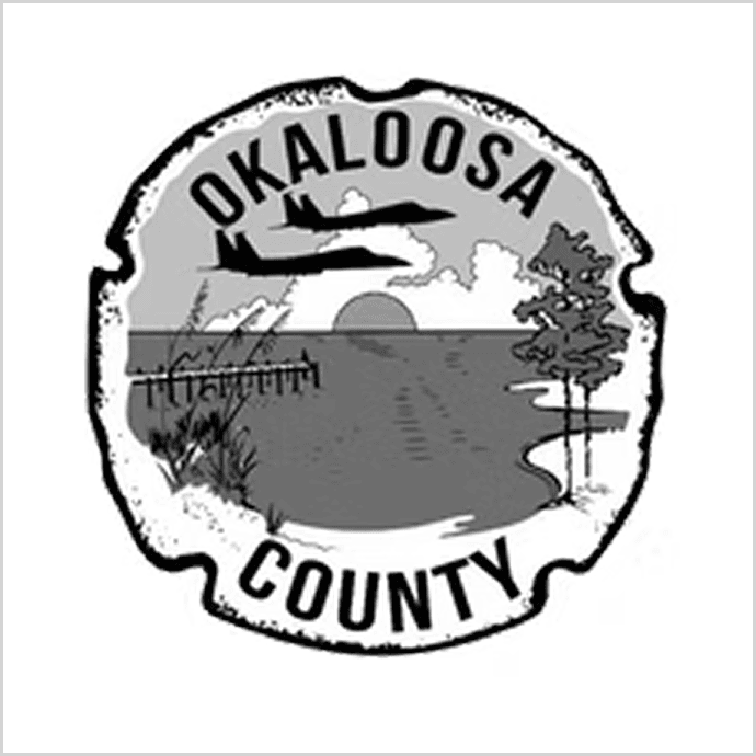 Okaloosa County logo, which consists of a black and white picture of trees, water, a bridge, and the sun