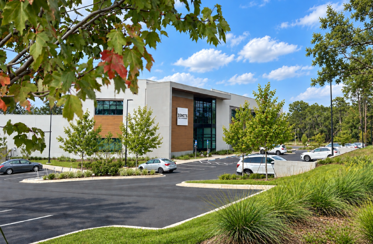 Building with glass windows and a name board, surrounded by a parking lot with cars parked in front of it